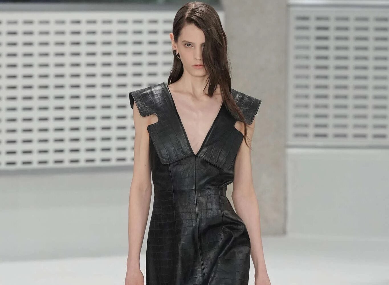 Modelo luciendo un vestido midi de cuero negro con textura de cocodrilo, escote en V pronunciado y hombros estructurados.