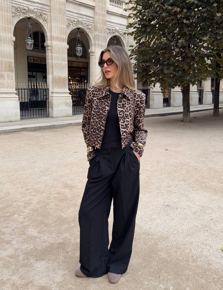 Mujer posando en la calle con una chaqueta corta de estampado de leopardo, top negro, pantalones sastre amplios de tiro alto y gafas de sol.