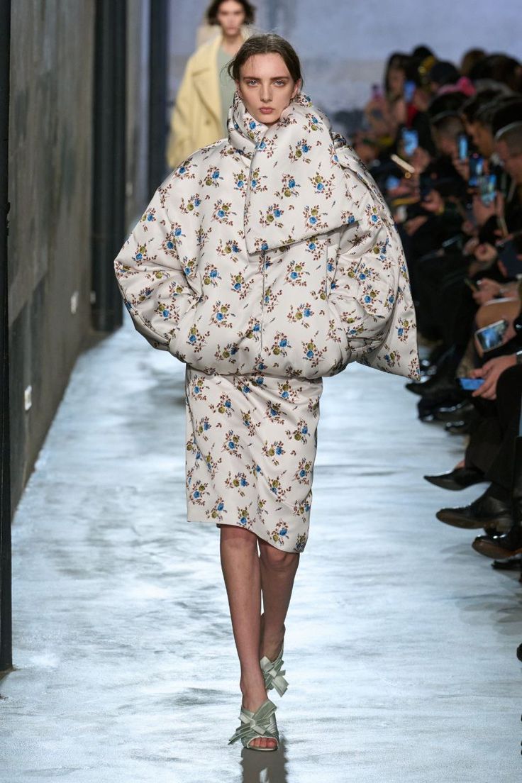 Modelo en pasarela luciendo un conjunto acolchado de chaqueta bomber extragrande y falda a juego con estampado de pequeñas flores azules y verdes sobre fondo blanco.
