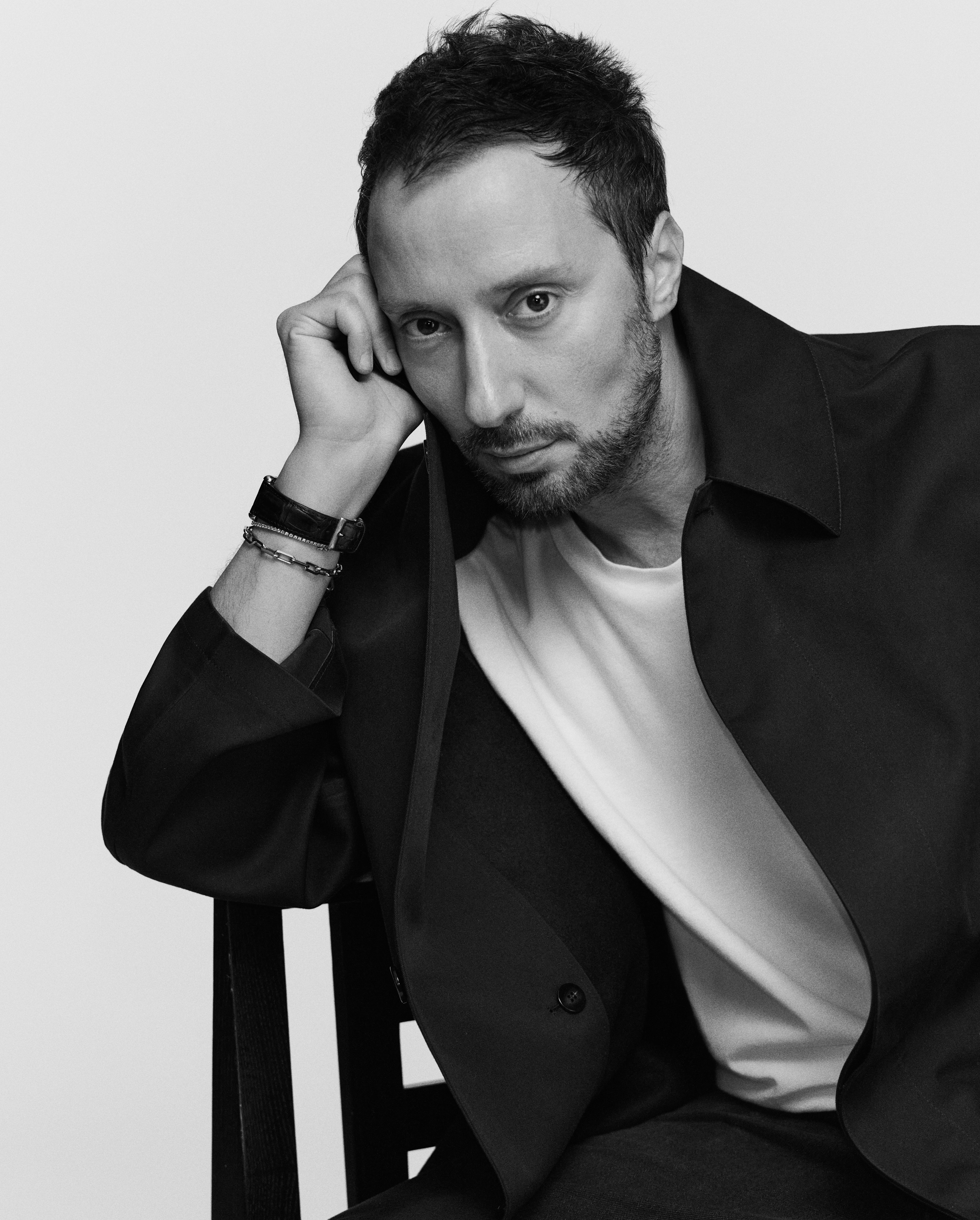 Retrato en blanco y negro de Anthony Vaccarello apoyando la cabeza en su mano, vistiendo una chaqueta oscura y una camiseta blanca.