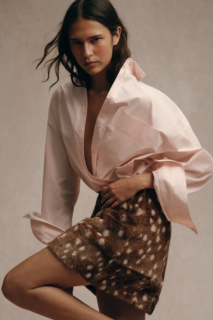 Modelo en un retrato de estudio vistiendo una camisa oversize de color rosa claro desabotonada y una falda corta con estampado de bambi en tonos marrones.