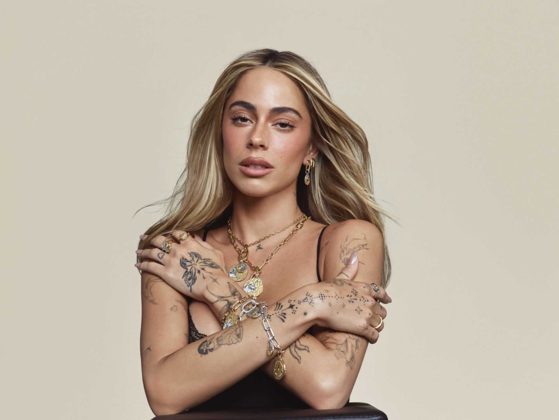 Tini en un plano medio con una ligera inclinación de cabeza, destacando su mirada y el juego de joyería superpuesta en capas con dijes inspirados en la astrología.