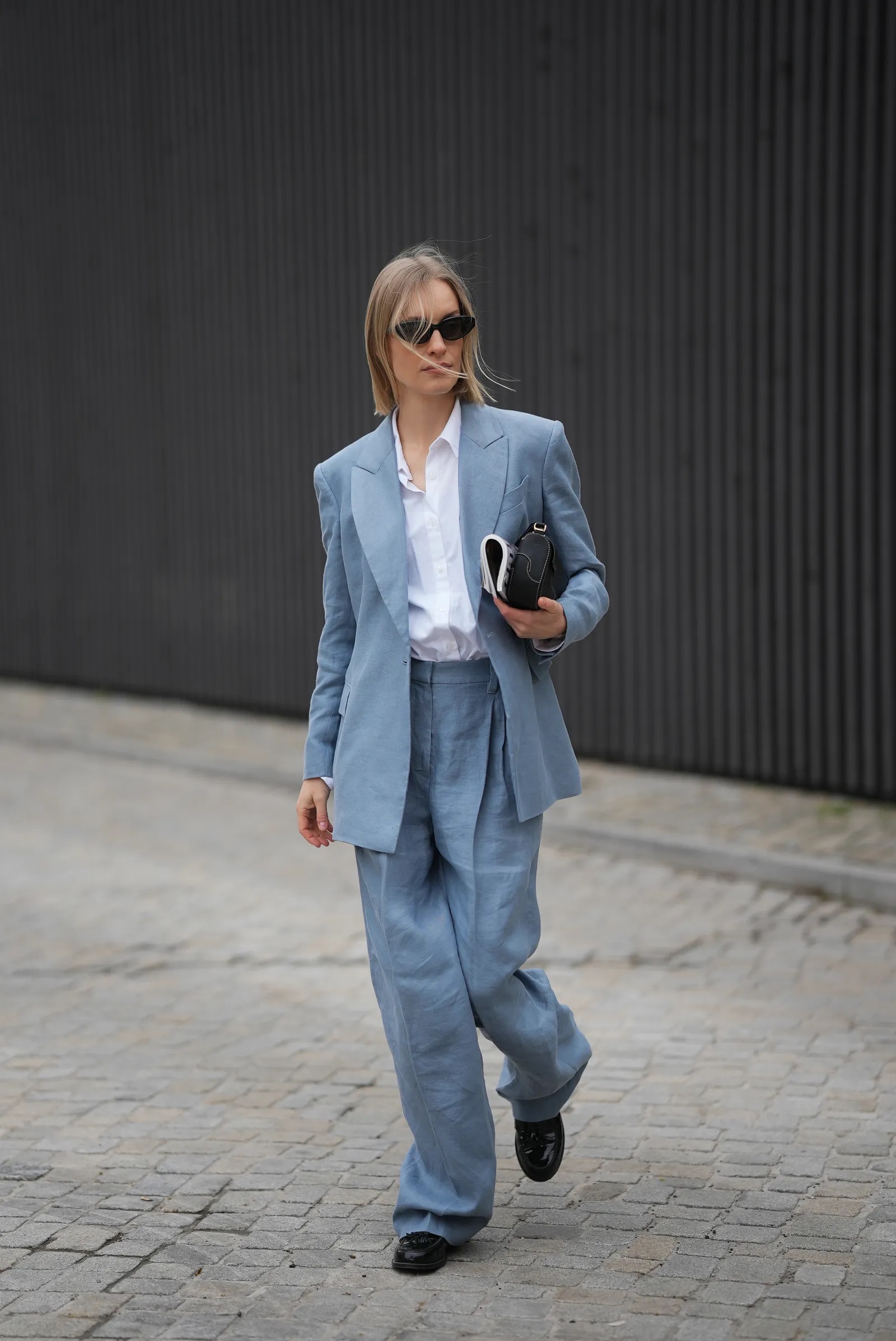 Mujer desfilando con un traje sastre amplio de lino en tono azul cielo, camisa blanca clásica y mocasines oscuros con borlas.