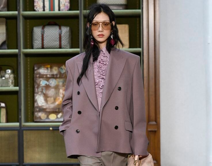 Modelo luciendo una chaqueta oversized de tweed a cuadros en tonos grises y beige, sobre un vestido largo vaporoso en tono rosa suave y lavanda, con accesorios sutiles.