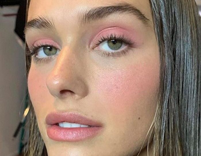 Primer plano de una modelo con cabello largo y oscuro, luciendo un maquillaje monocromático en tonos rosa suave tanto en los párpados como en las mejillas y los labios.
