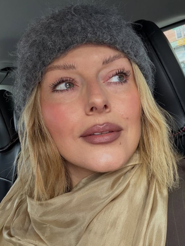 Mujer rubia con un gorro de punto gris oscuro y bufanda dorada, mostrando un maquillaje en tonos tierra con labios definidos mediante el estilo halo lips.