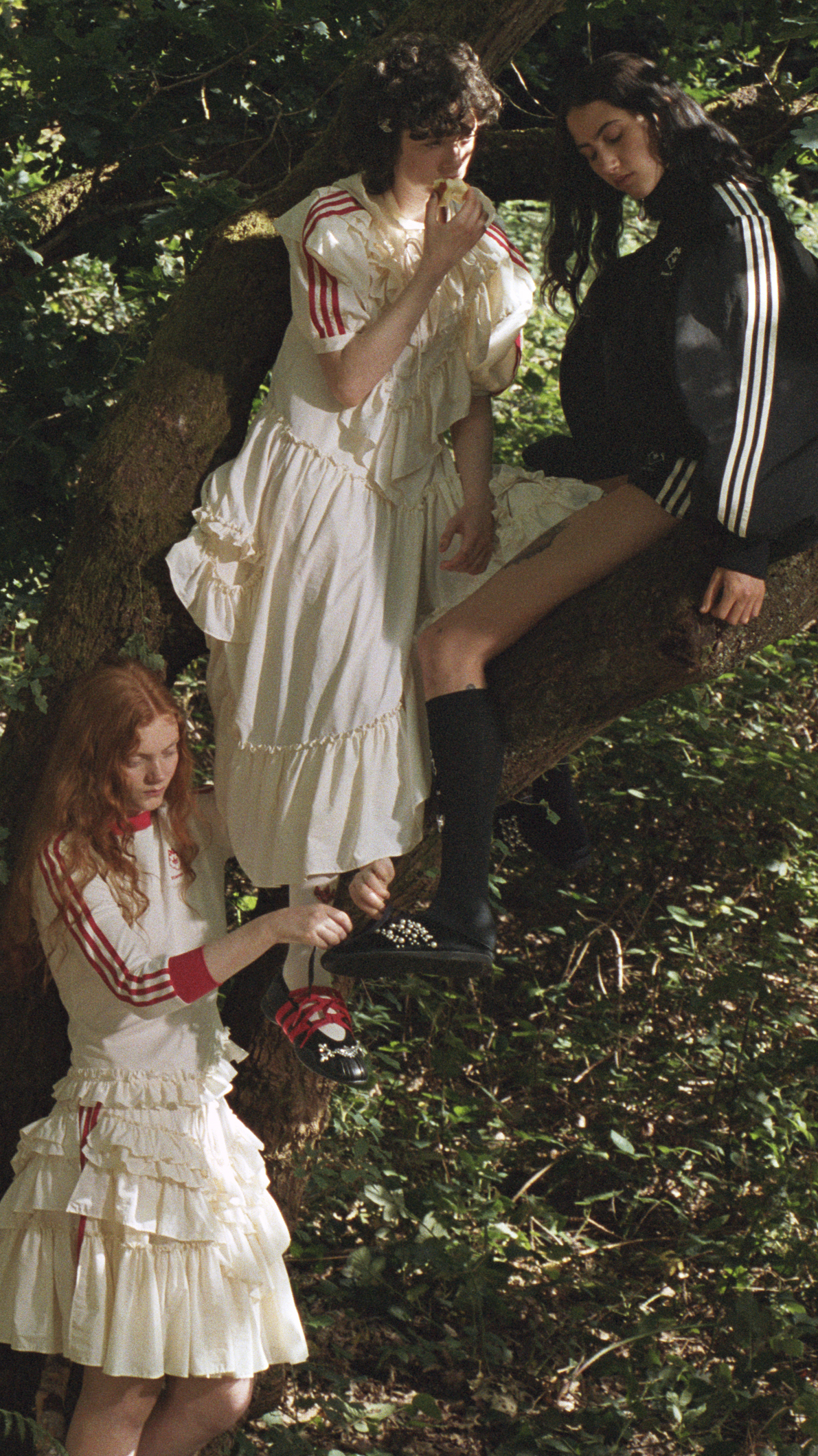 Escena en un bosque donde tres modelos interactúan entre los árboles; una de ellas lleva un vestido blanco de volantes y calza zapatillas adornadas con perlas.