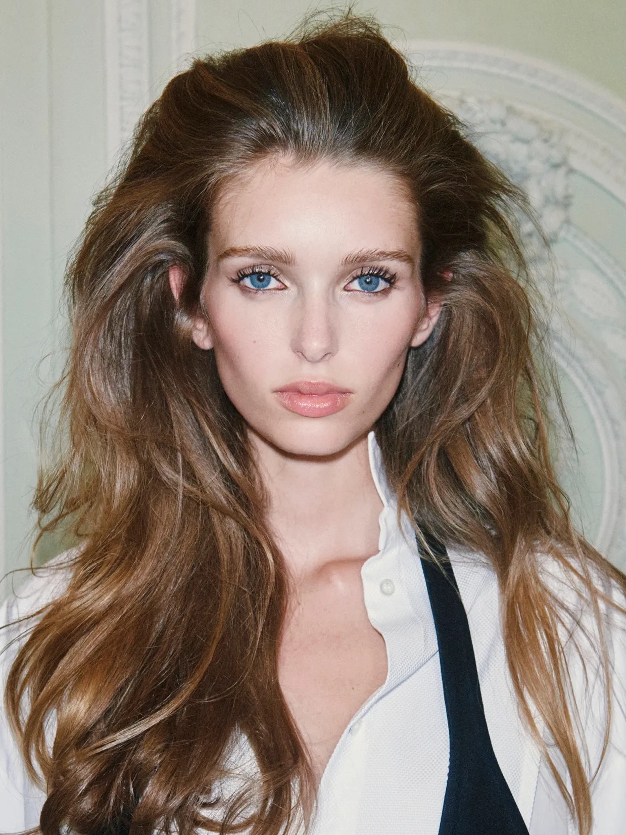 Modelo de cabello castaño largo con volumen texturizado en la coronilla estilo semirrecogido y una blusa blanca clásica.