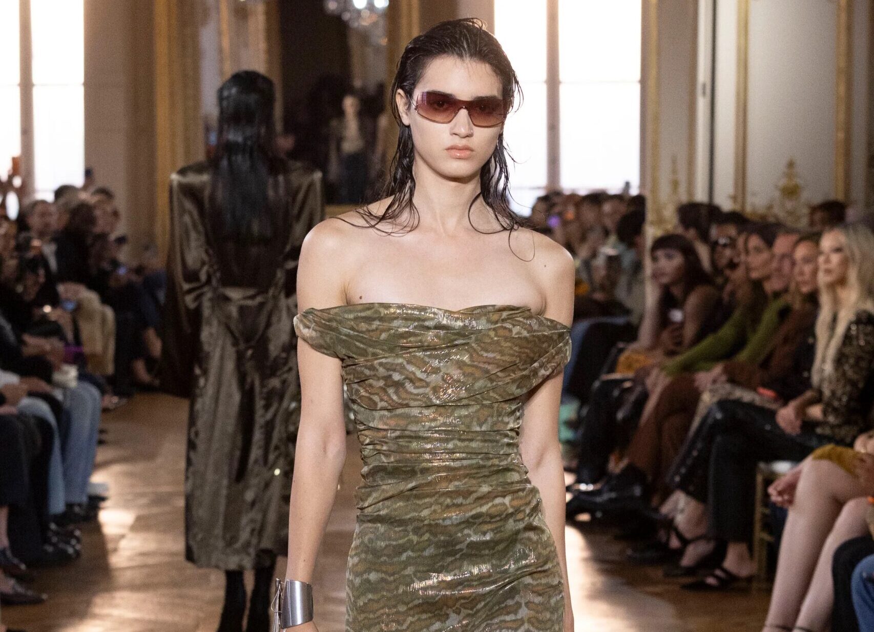 Modelo luciendo un vestido midi strapless con estampado orgánico difuminado en tonos tierra y metálicos, acompañado de gafas de sol oscuras y un bolso de mano a juego.