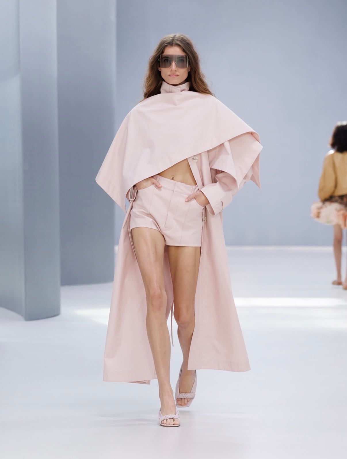 Modelo con lentes grandes y capa larga con shorts rosas