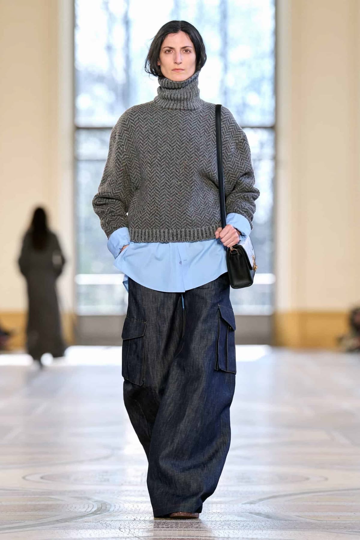 Modelo con pantalones cargo, camisa azul y suéter gris