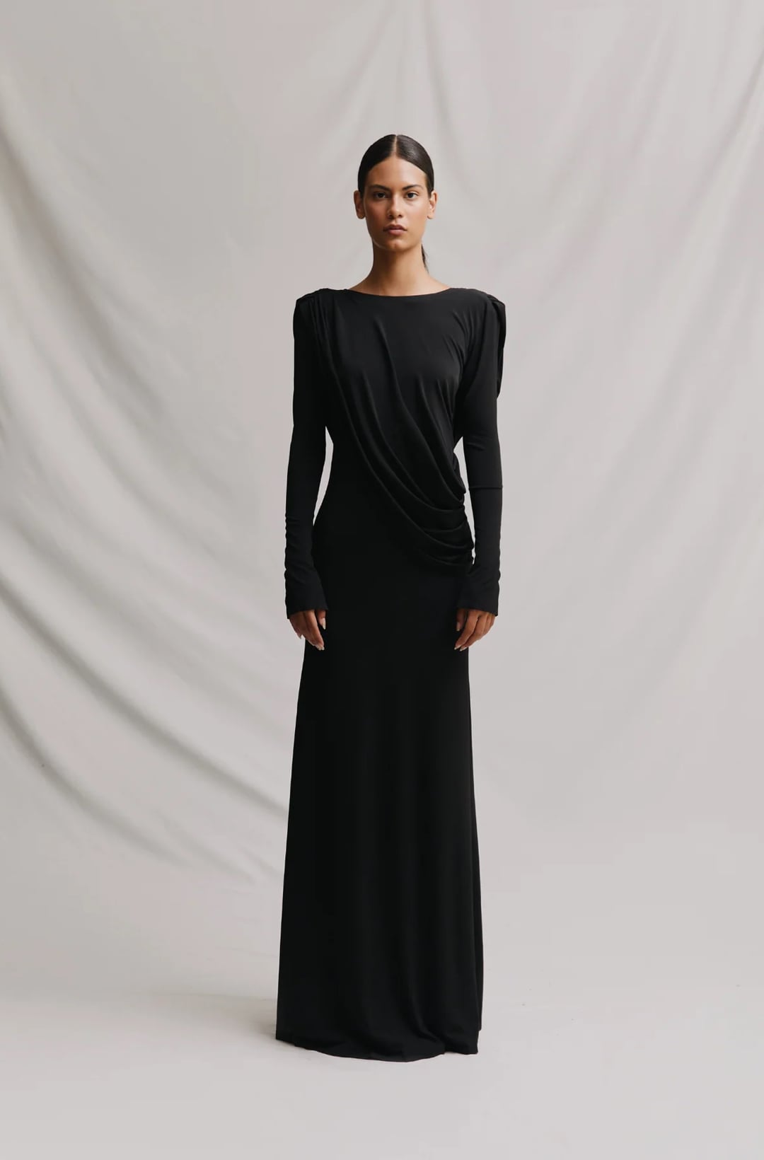 Fondo blanco con mujer llevando un vestido negro con hombreras y manga larga