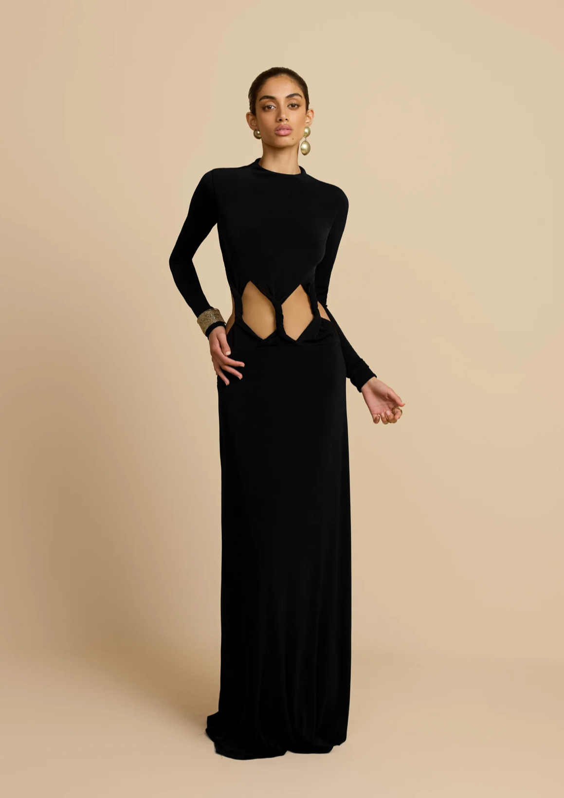 Color beige de fondo con modelo sobre un vestido negro con cut outs