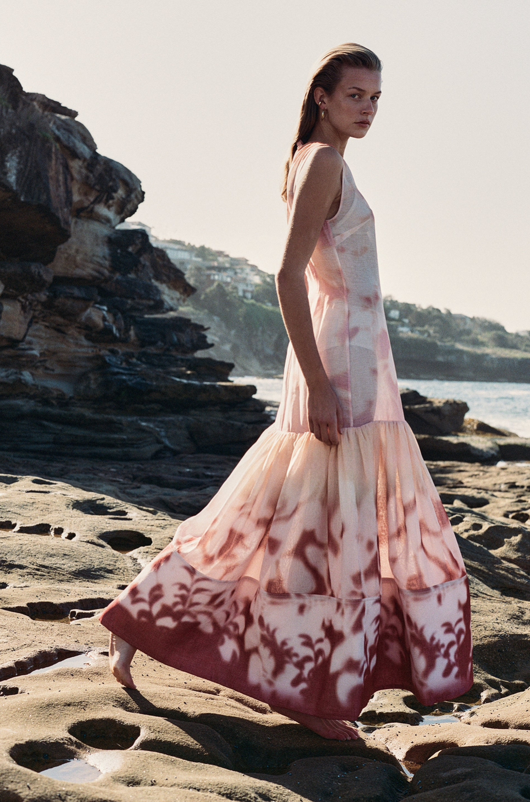 Playa de fondo con mujer caminando sobre la arena con vestido largo blanco con rosa