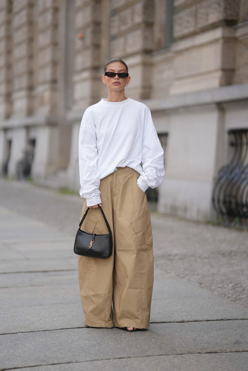 Calle borrosa de fondo con mujer en pantalones cargo beige con blusa blanca de manga larga