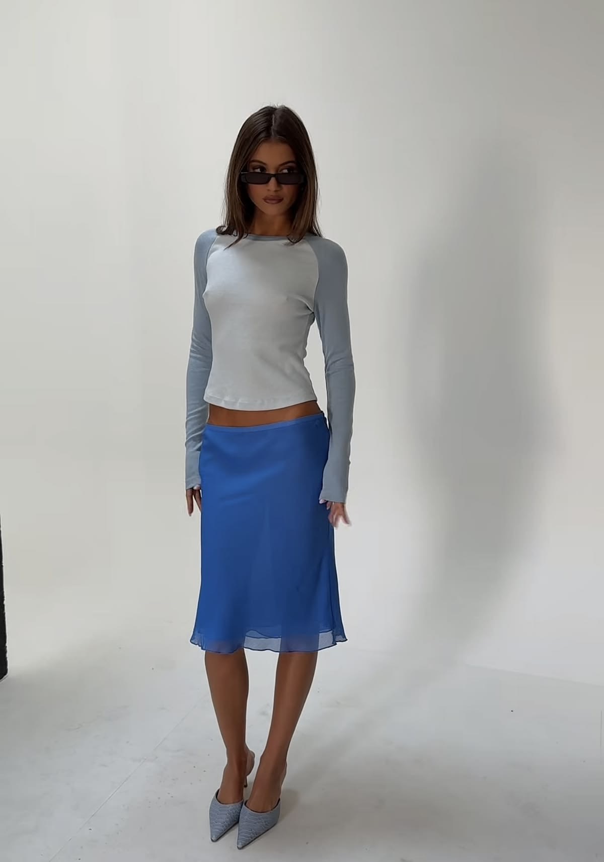 Fondo blanco con mujer posando con falda midi azul y baseball tee