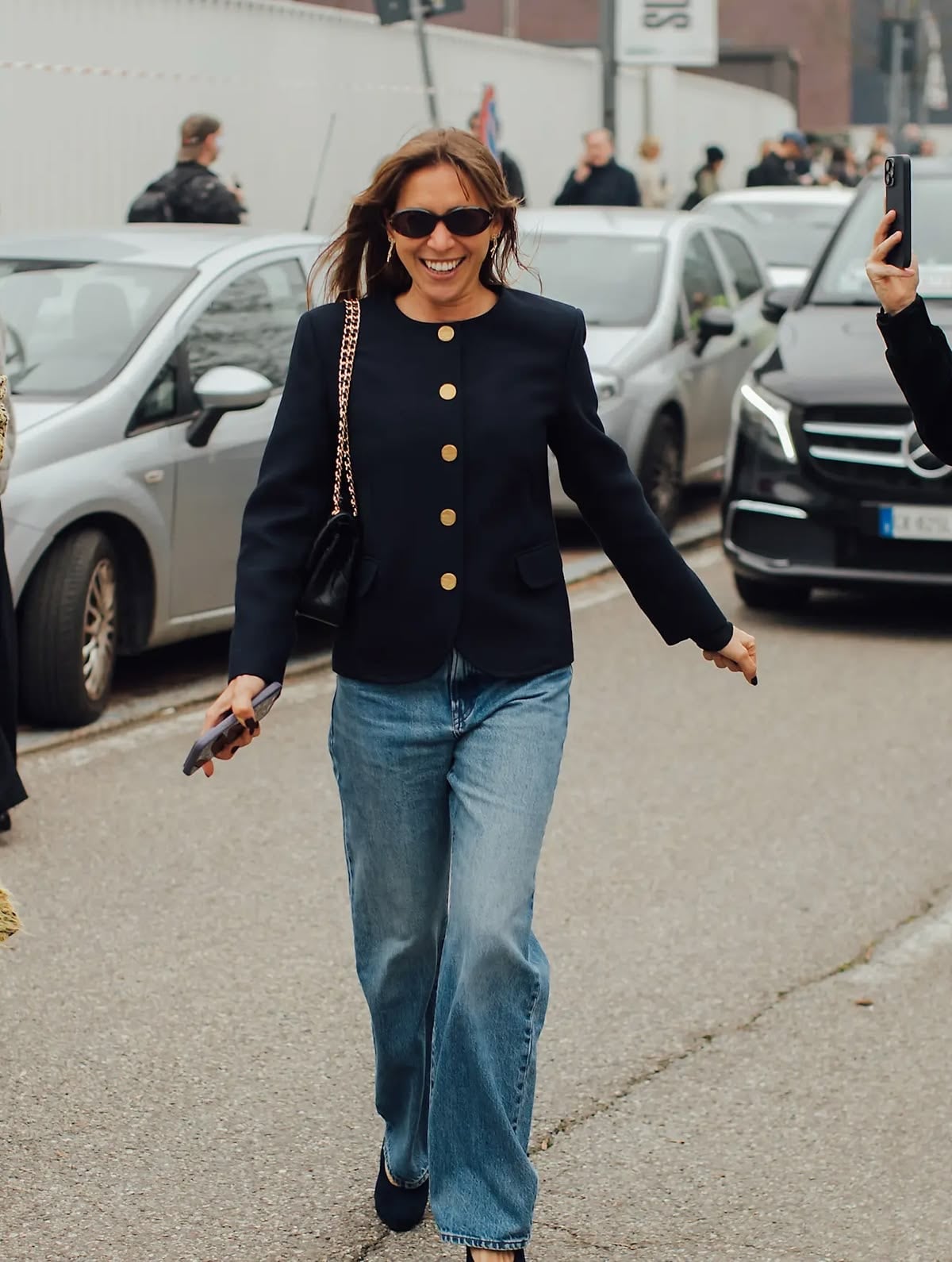 Coches detrás y mujer caminando en jeans con saco sin cuello azul