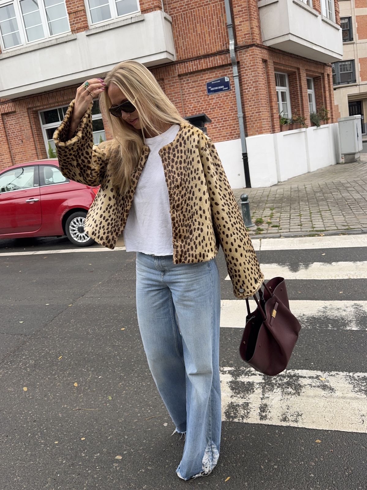 Mujer rubia caminando en la calle con jeans y chaqueta de animal print sin cuello