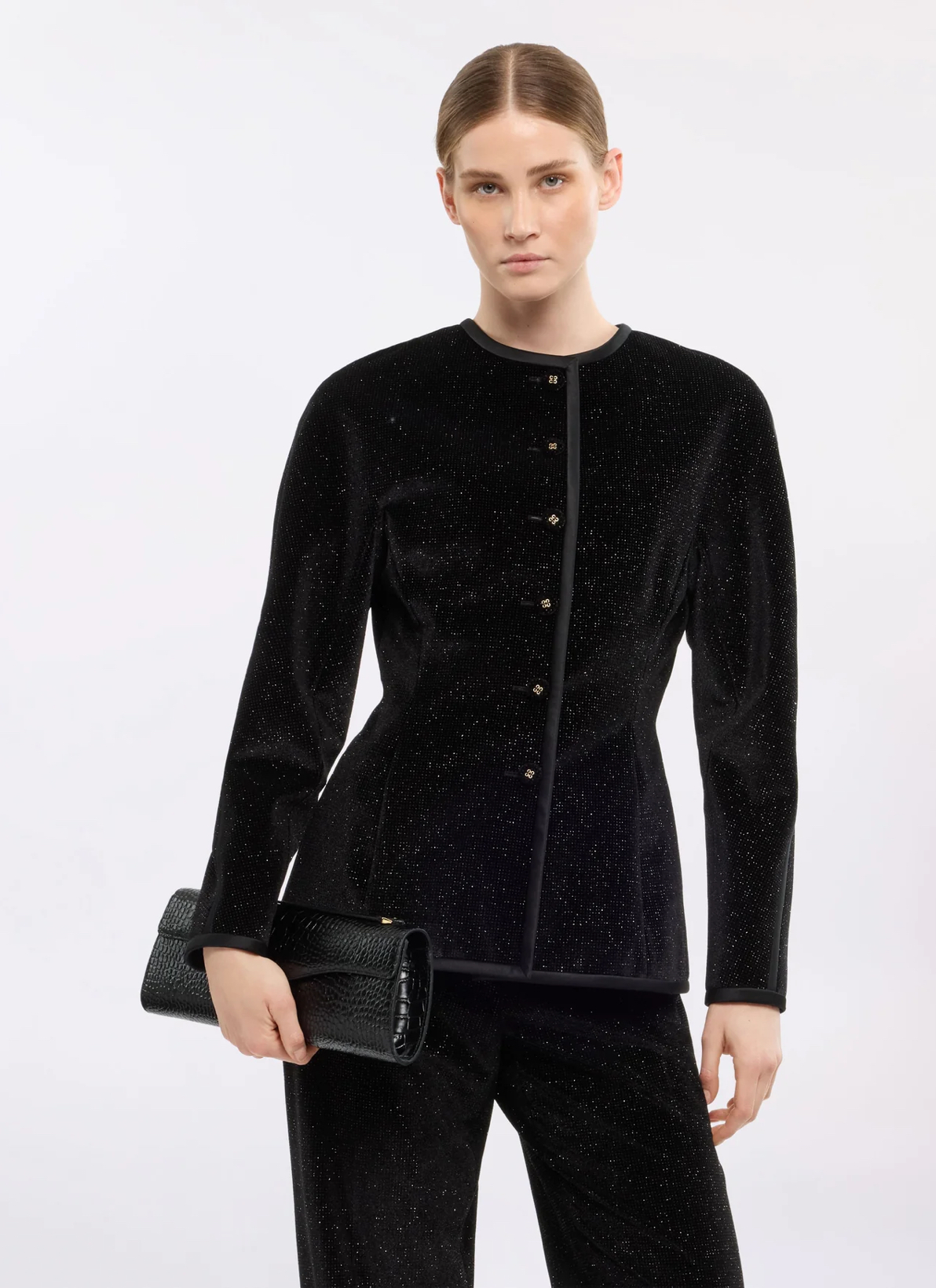 fondo blanco con modelo en saco sin cuello, pantalones y bolso negro