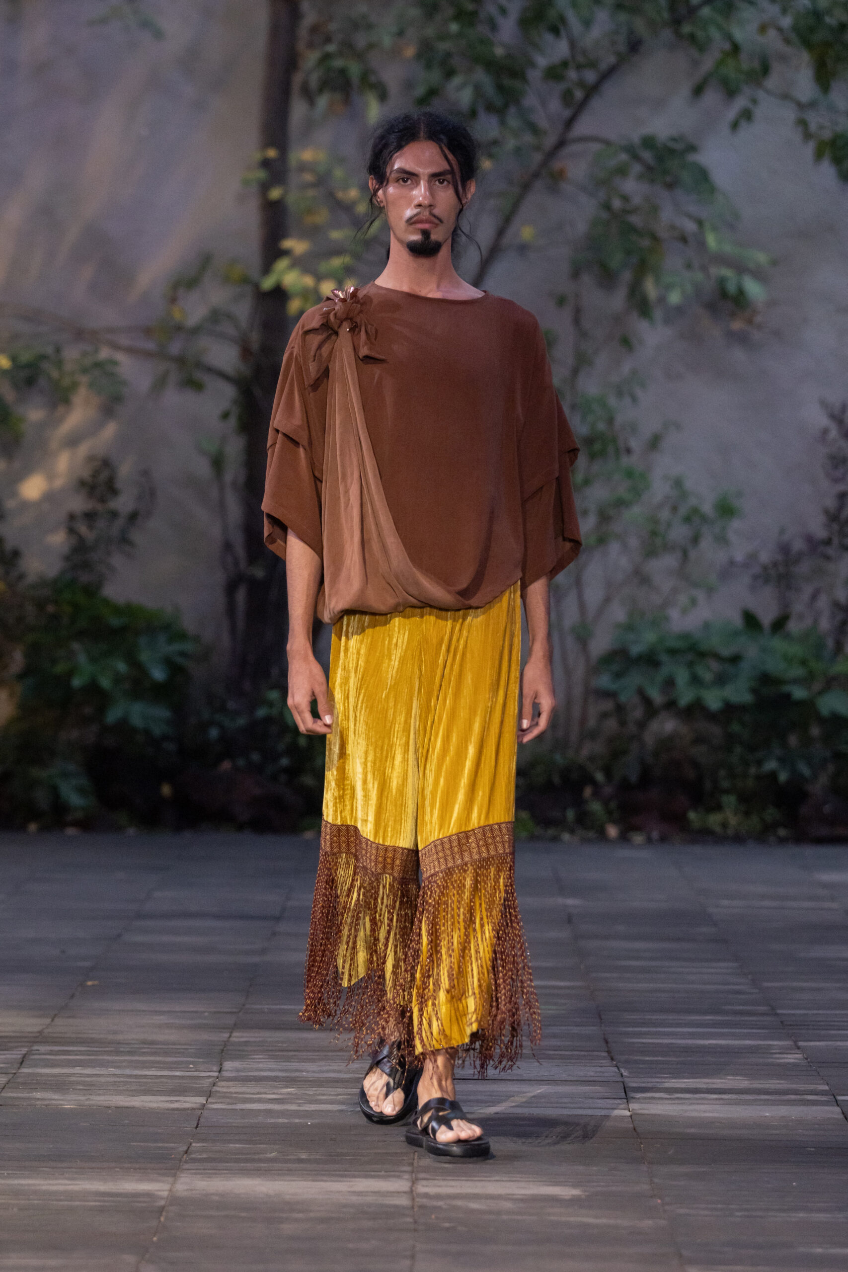 Mujer desfilando con pantalones amarillos con flecos de chaquira y blusa café Carla Fernández x KUU