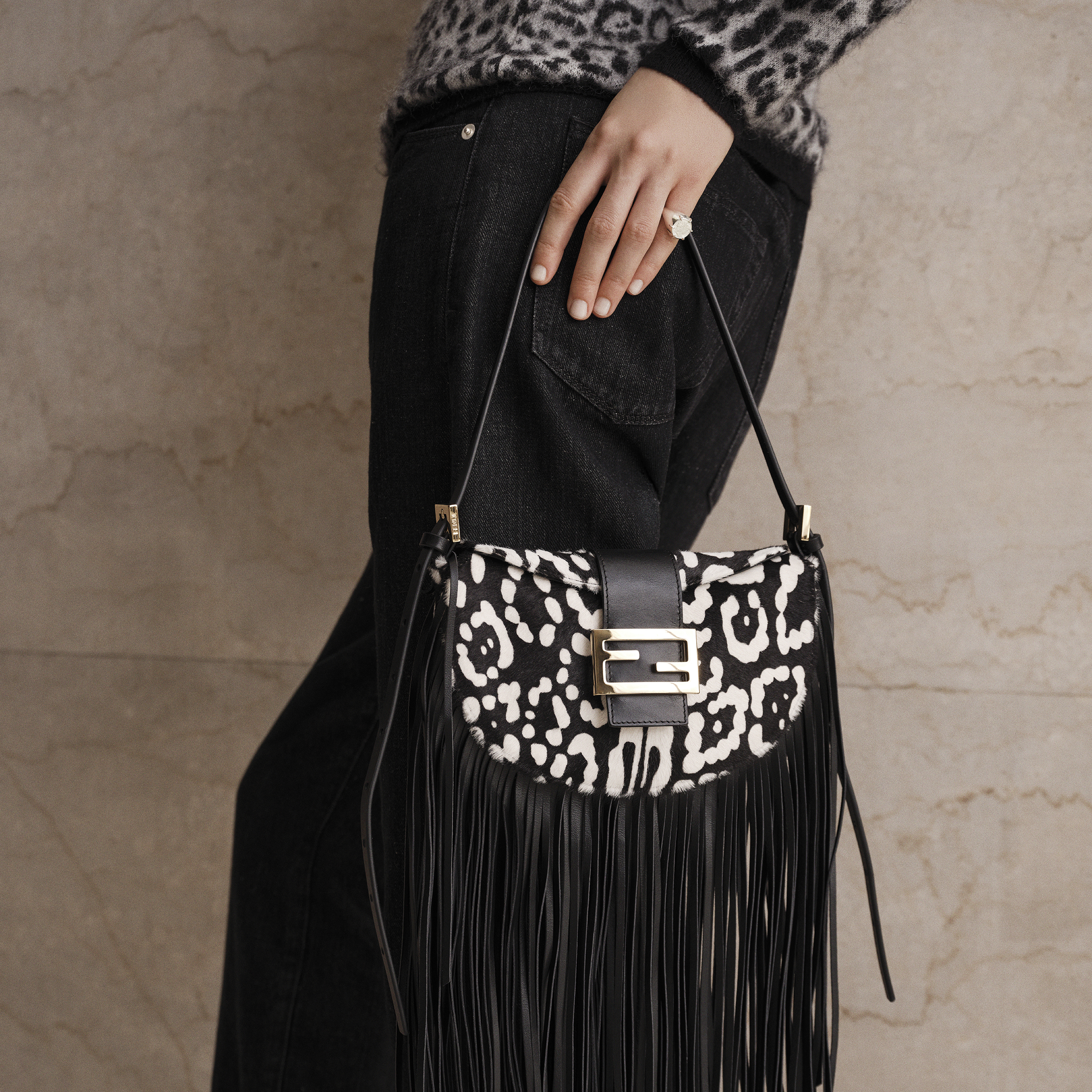 Mano sosteniendo un bolso animal print negro con blanco y flecos