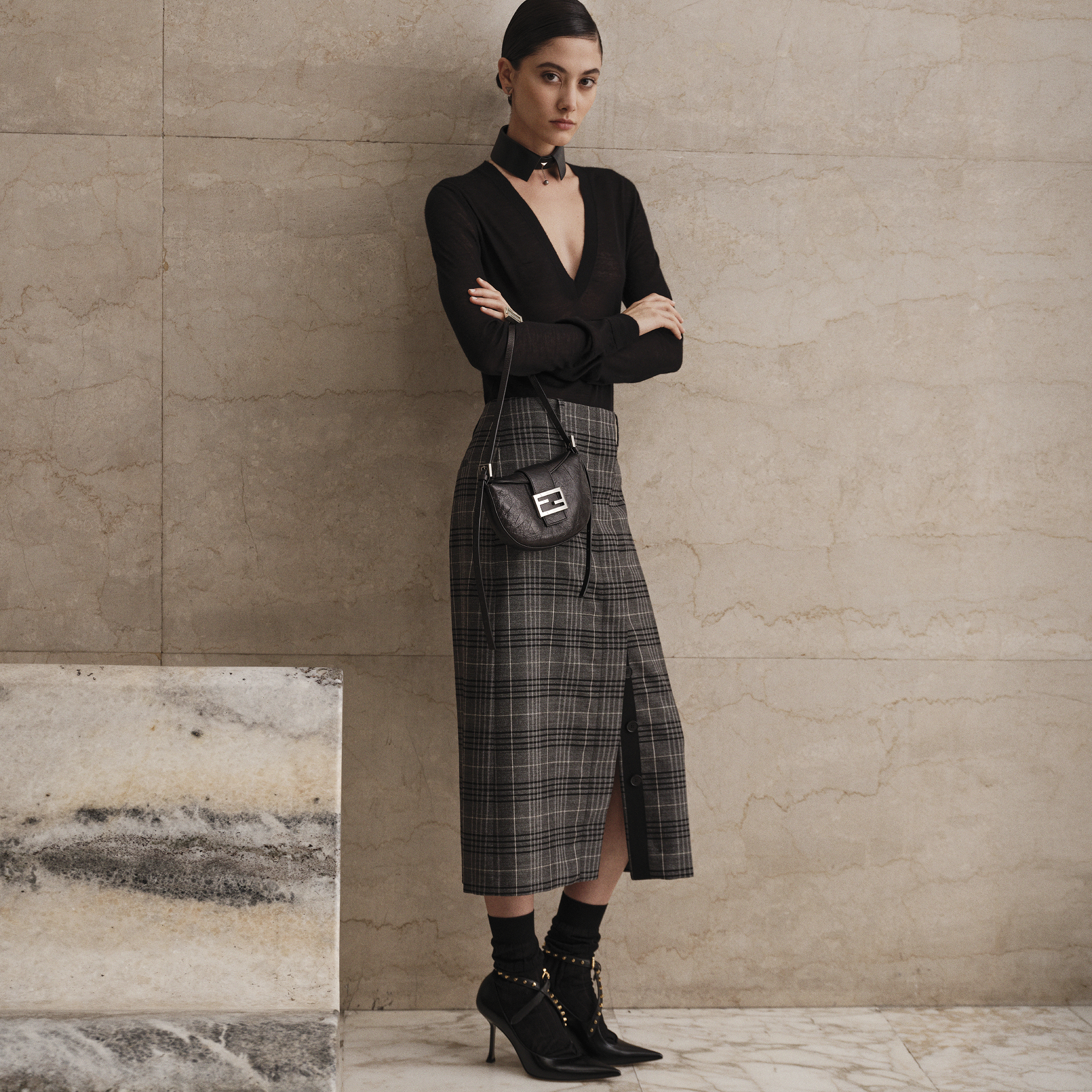 Modelo con falda de cuadros y blusa negra con bolso croissant negro de FENDI
