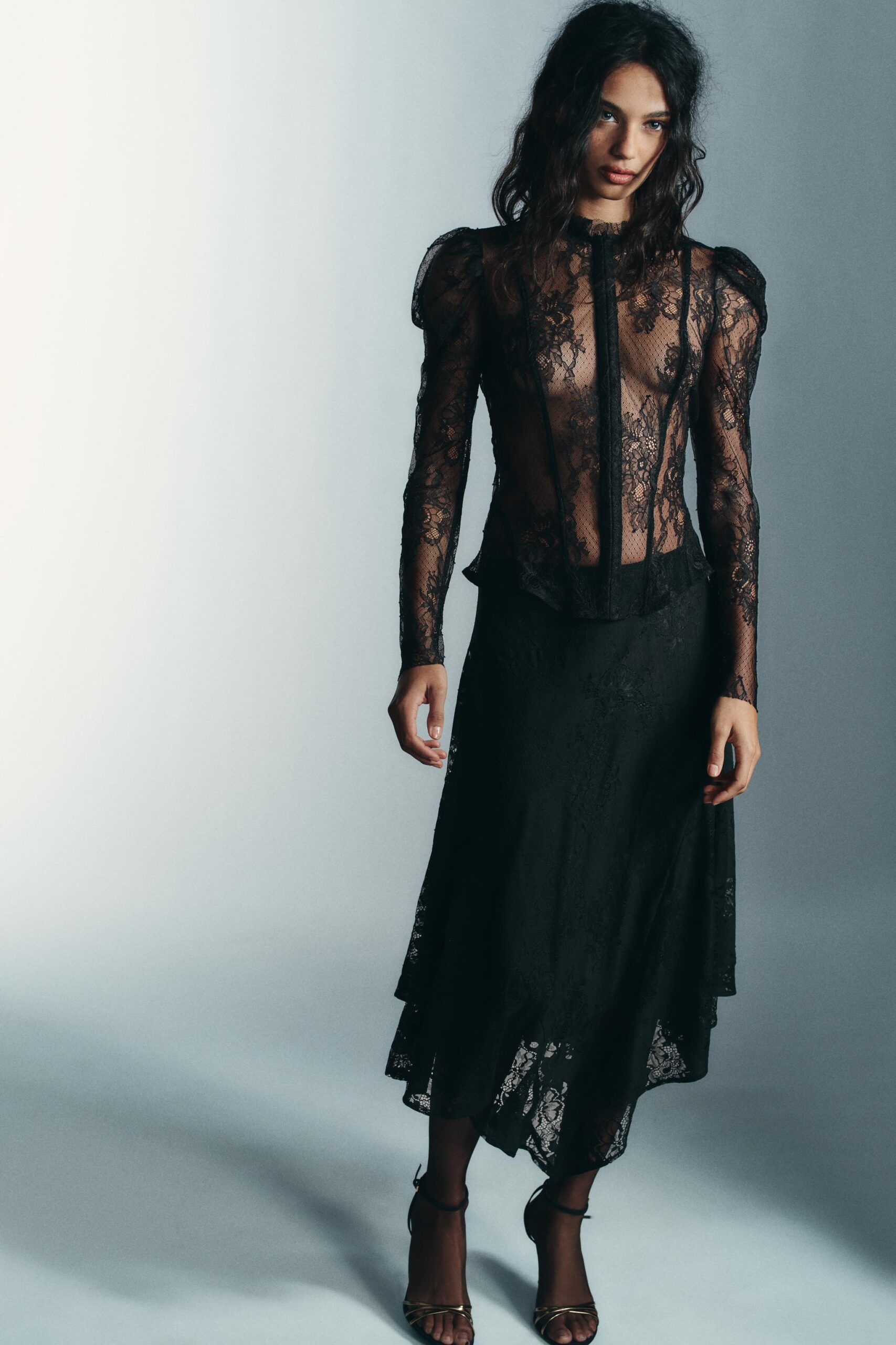 Fondo gris y modelo con falda negra de encaje y blusa negra de manga larga de encaje colección ZARA día de muertos