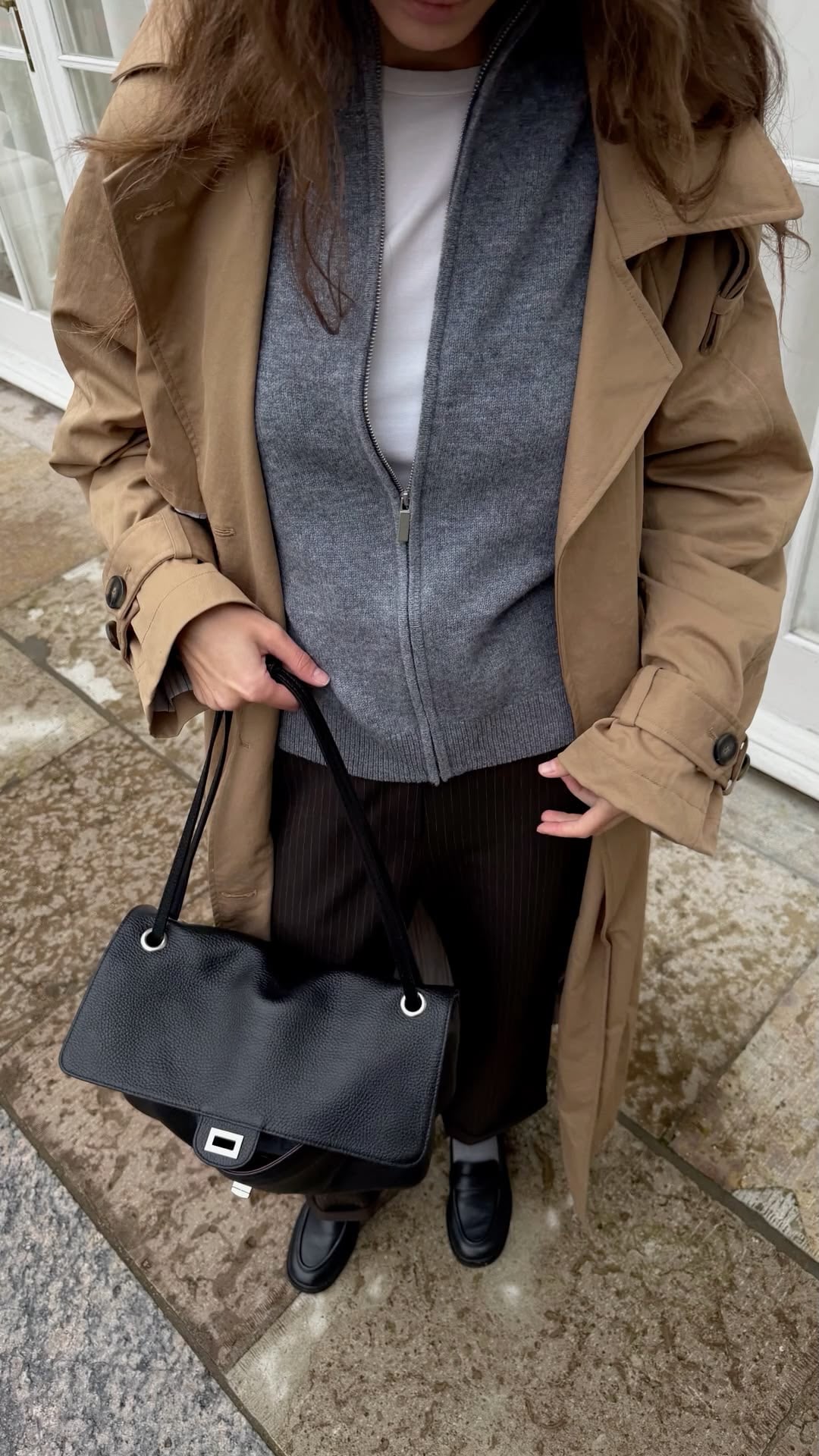 Foto en picada de mujer con blusa blanca, suéter gris y trench beige con bolso negro