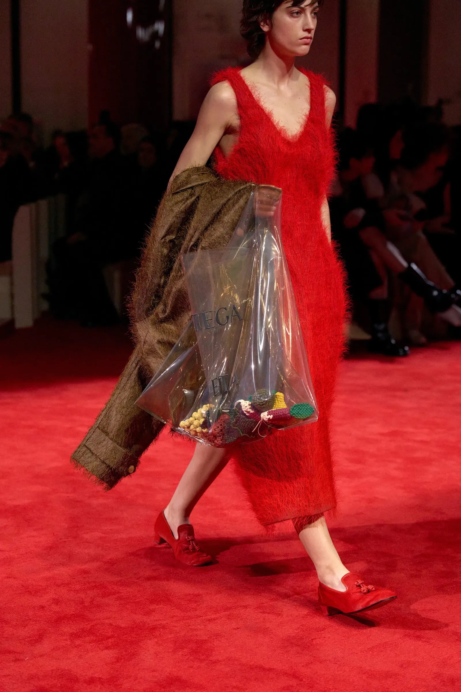 Modelo luciendo un vestido midi de textura peluda en color rojo intenso, acompañado de unos mocasines planos rojos a juego y un bolso transparente.