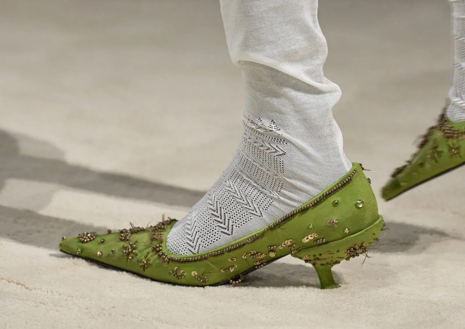 Detalle de unos zapatos de tacón sensato en color verde lima, adornados con intrincados bordados de pedrería, combinados con medias y leggins blancos.