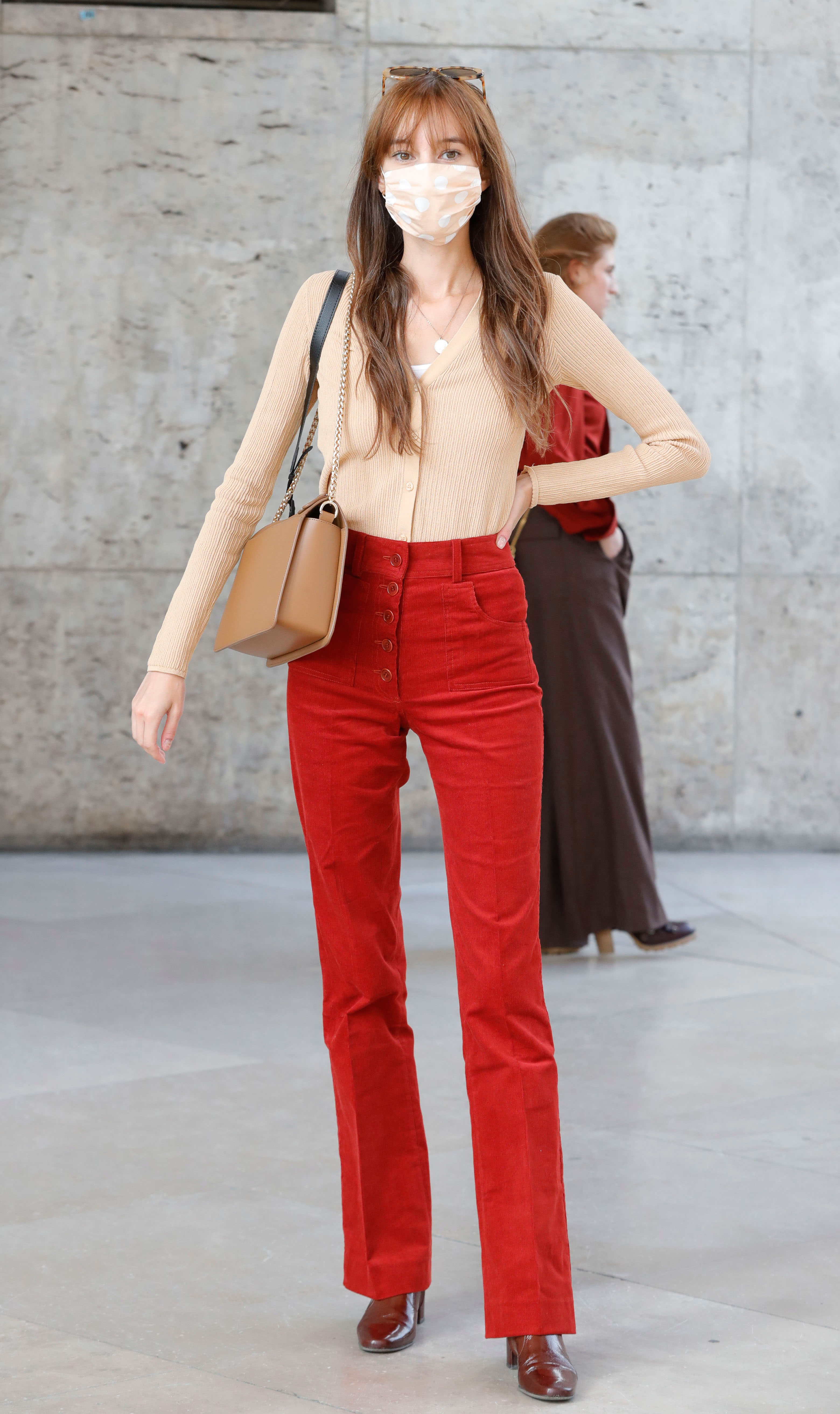 Paris Fashion Week Street Style: Woman wears a beige top, mask, and red high-waisted pants.