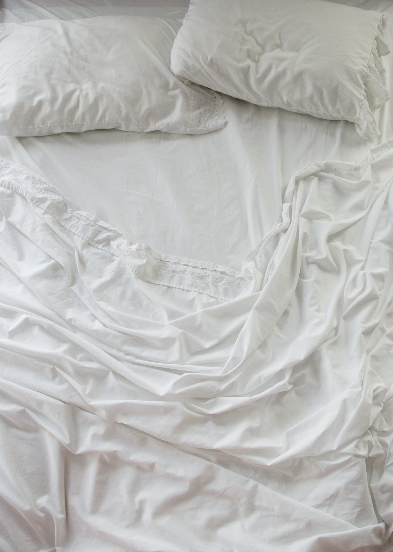 High Angle View of Unmade Bed with Rumpled White Sheets and Two Pillows in Soft Early Morning Light