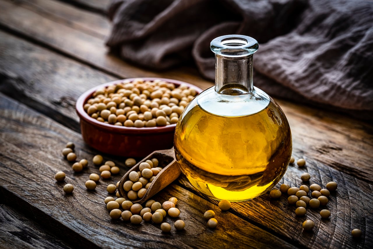 Close up view of a glass bottle filled with soy oil shot on rustic wooden table. A bowl with dried soybeand complete the composition Plant-based nutrition concept. High resolution 42Mp studio digital capture taken with Sony A7rII and Sony FE 90mm f2.8 macro G OSS lens