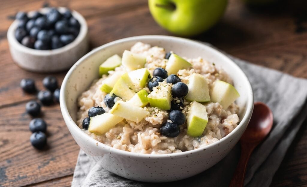 Healthy breakfast food: oatmeal porridge with green apple, blueberries, and hemp seeds.