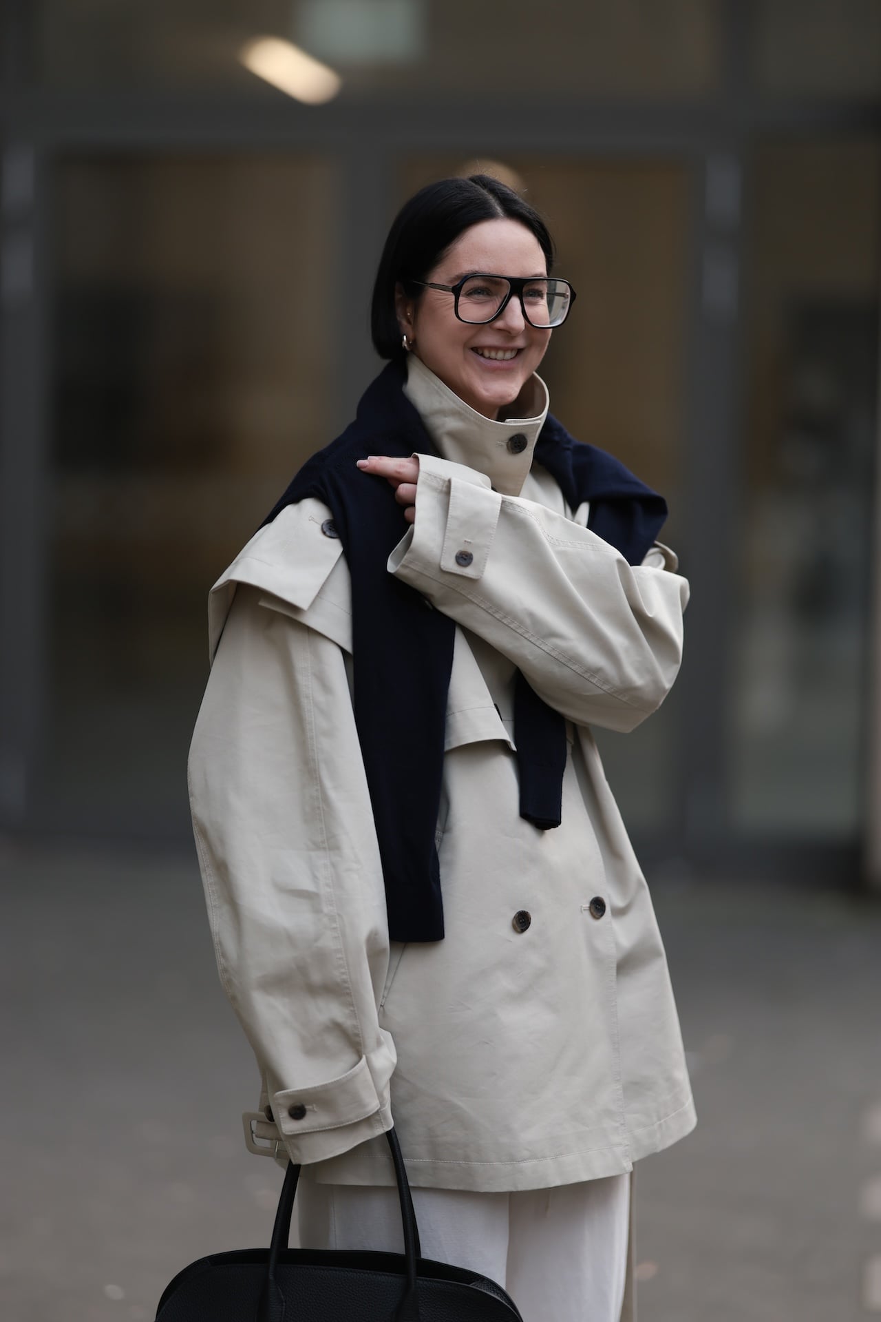 DUESSELDORF, GERMANY - MARCH 06: Maria Barteczko is seen wearing a dark brown straight bob haircut and wears large black oversized Aviator optical glasses by Victoria Beckham. She is dressed in a beige funnel-neck cropped trench coat from Front Row Shop, layered over a blue over-the-shoulder cashmere knit from COS, and white linen wide-leg pants, also from COS. She carries a large black Margaux leather bag from The Row and wears black leather ballerinas from The Row, creating a modern, minimalist, and chic look on March 06, 2026 in Duesseldorf, Germany. (Photo by Jeremy Moeller/Getty Images)