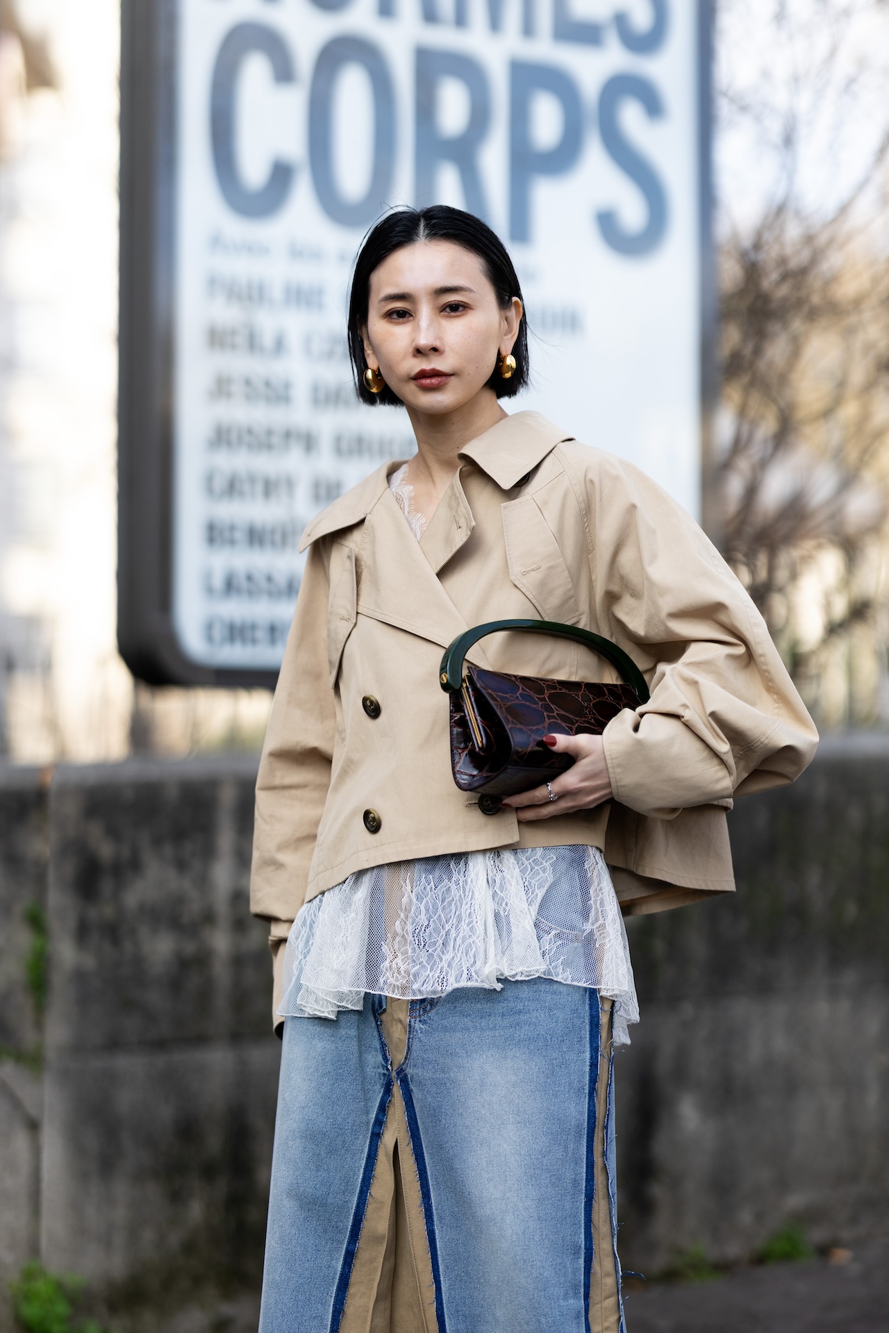PARIS, FRANCE - MARCH 10: A guest wears a beige and denim midi high waist skirt, a white lace top, a brown leather bag, gold hoop earrings and a beige cropped trench outside Ujho show during Day Nine of Paris Fashion Week - Womenswear Fall/Winter 2026/2027 on March 10, 2026 in Paris, France. (Photo by Valentina Frugiuele/Getty Images)