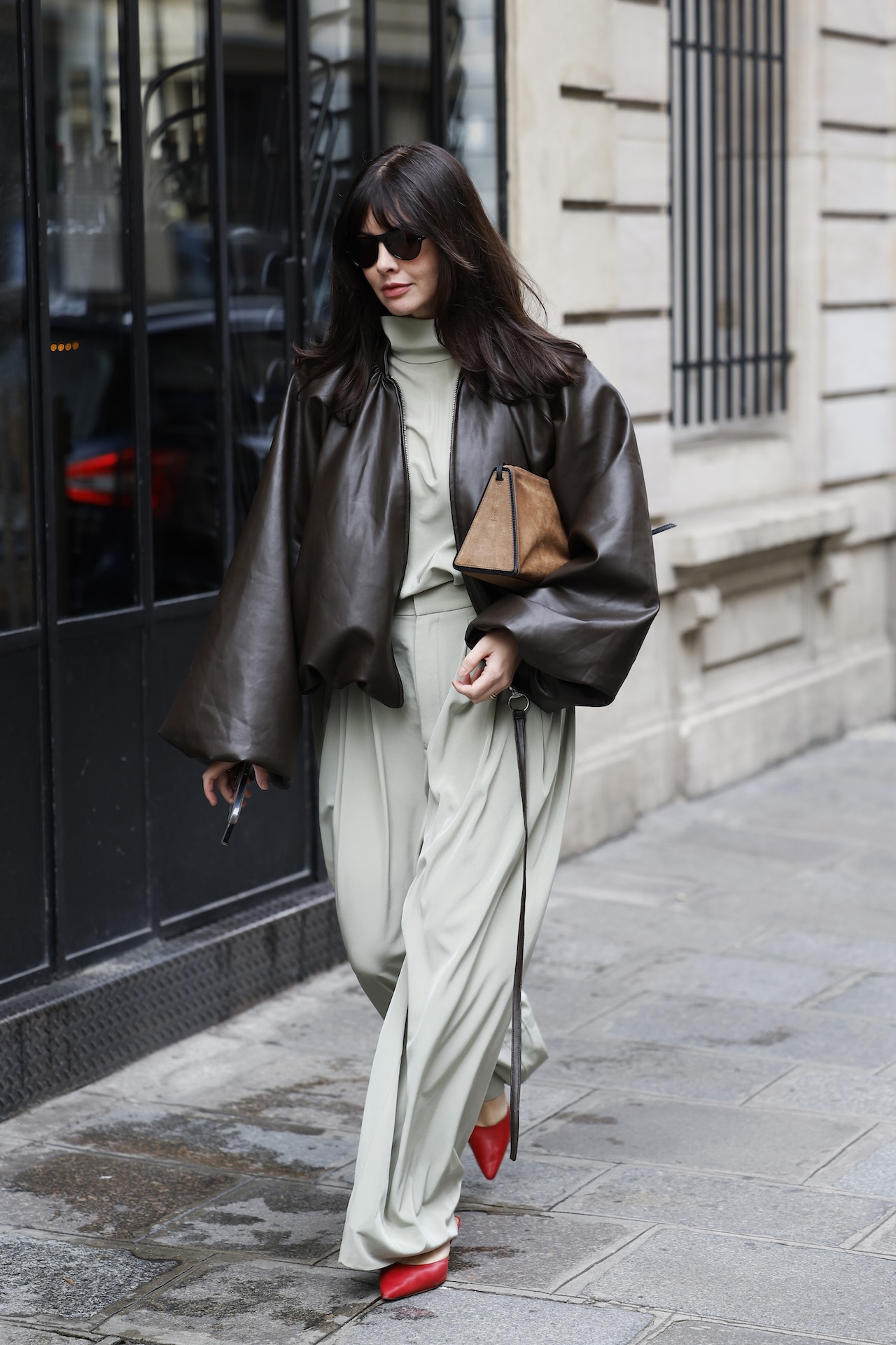 PARIS, FRANCE - OCTOBER 06: A guest wears light green blouse, matching trousers, brown leather bomber jacket, beige suede bag, red heels, outside Sacai, during the Womenswear Spring Summer 2026 as part of Paris Fashion Week on October 06, 2025 in Paris, France. (Photo by Claudio Lavenia/Getty Images)