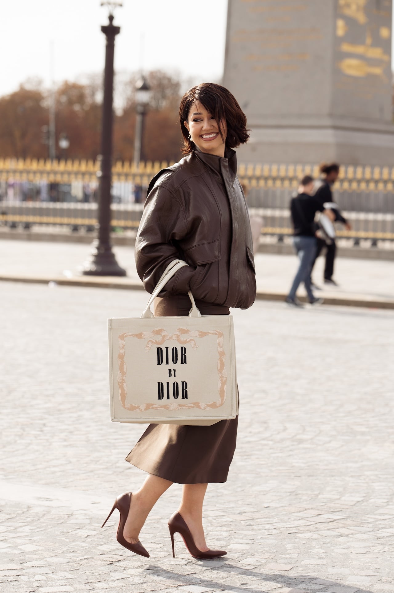 PARIS, FRANCE - OCTOBER 01: Lena Mahfouf wears a brown leather bomber jacket over a brown midi skirt, styled with burgundy pointed heels and a large Dior by Dior canvas tote outside Dior show during the Womenswear Spring Summer 2026 as part of Paris Fashion Week on October 01, 2025 in Paris, France. (Photo by Raimonda Kulikauskiene/Getty Images)