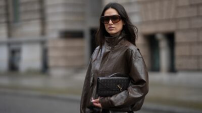 BERLIN, GERMANY - OCTOBER 22: Amanda Azoitei is seen wearing a dark brown oversized leather bomber jacket with a high collar and contrast stitching by The Frankie Shop;a dark brown woven leather clutch with a gold metal clasp by Bottega Veneta; oversized rectangular sunglasses with a gradient tint and brown frame by Gigi Studios; her long dark brown hair is worn straight and loose on October 22, 2025 in Berlin, Germany. (Photo by Moritz Scholz/Getty Images)