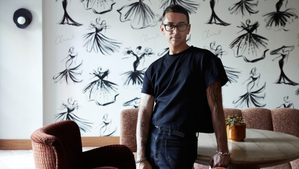 Pictured: Christian Siriano in the lobby of the Delamar Westport with the signature Siriano Sketch Wall behind him; Photo credit: Tim Lenz
