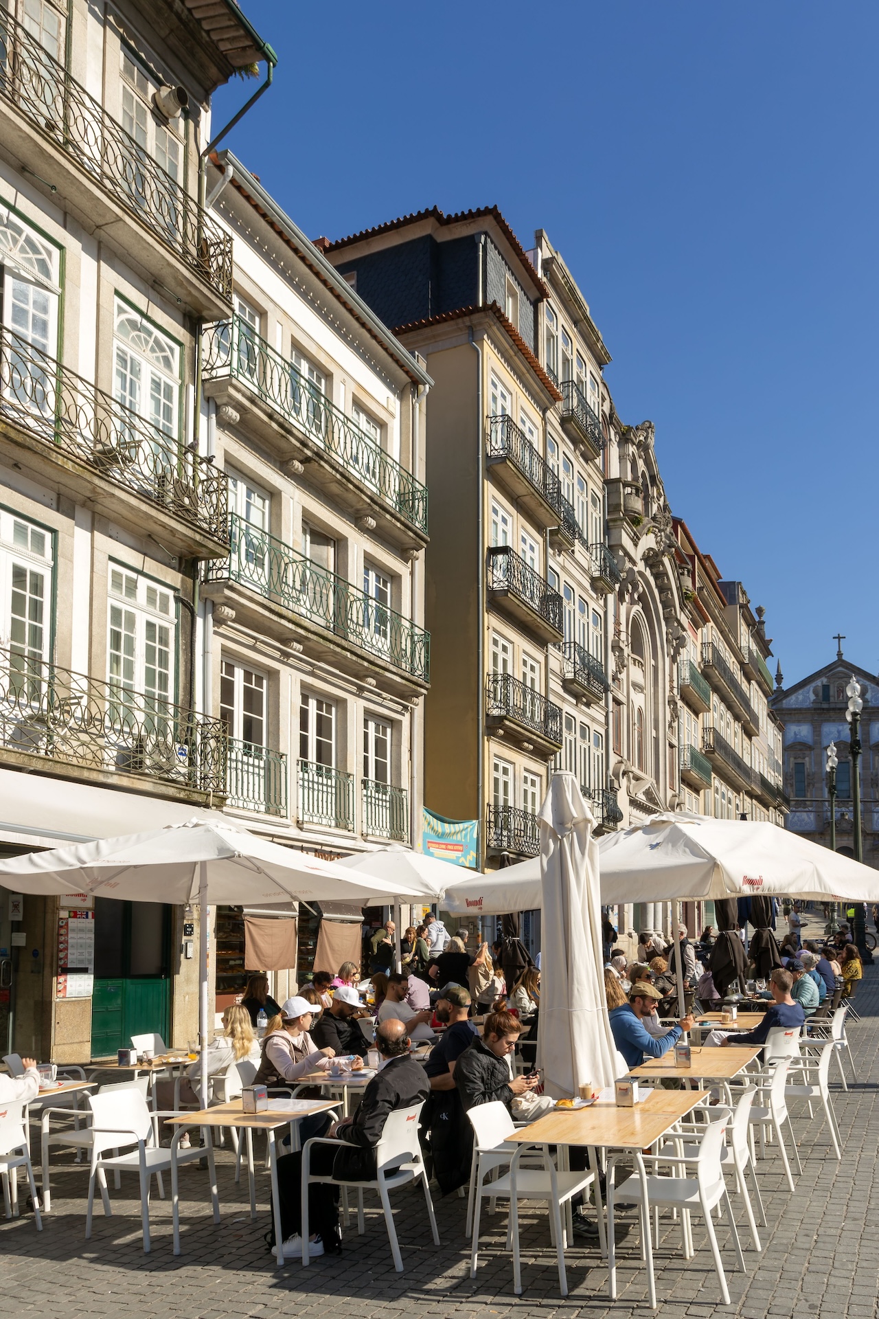 People sitting at cafe tables outside historic buildings, Praça de Almeida Garrett, Rua das Flores, Porto, Portugal, Europe. (Photo by: Geography Photos/Universal Images Group via Getty Images)