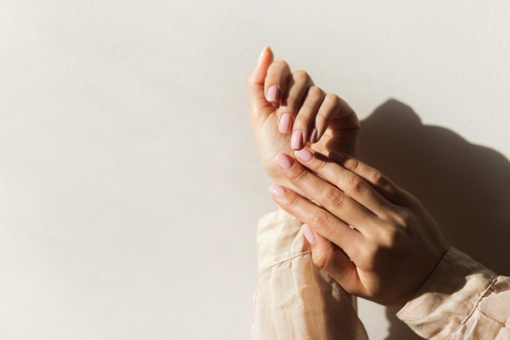 Manicure on female hands with light pink nail polish.