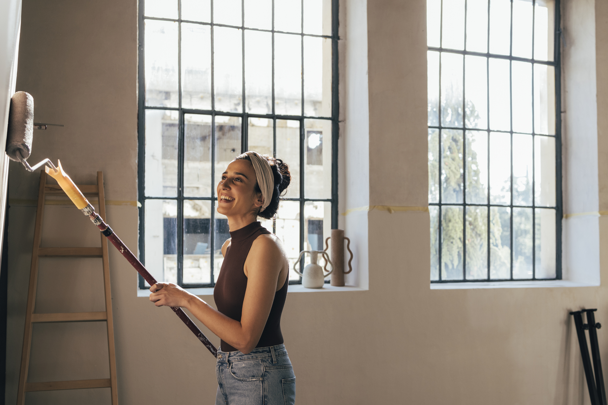 Smiling female person painting wall in light brown color with paint roller
