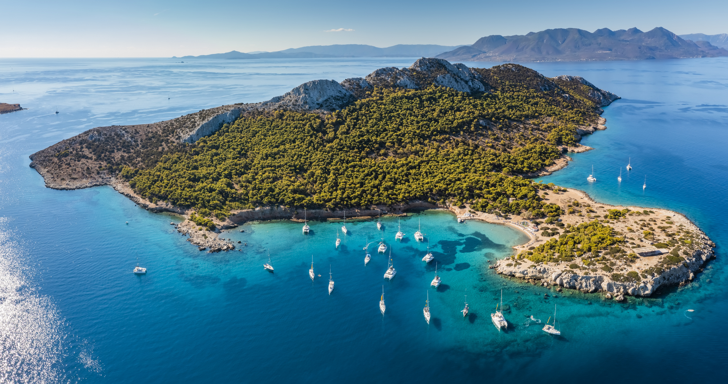 Yachts in turquoise water near the green island of Moni Eginas, Greece. Aerial view